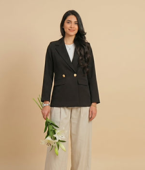 Woman wearing a black blazer and beige pants holding flowers against a beige background